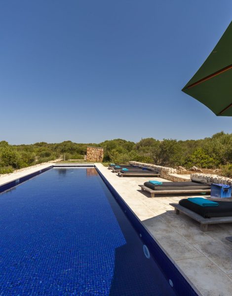 piscina de una villa de lujo en alquiler con comedor exterior y un amplio jardín.